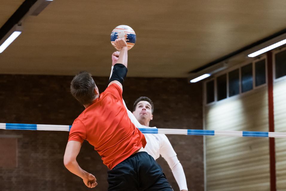 Zwei Spieler im Sprung während eines Handballspiels, einer wirft den Ball über eine Markierung.